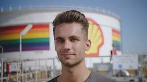 A male Shell employee standing in front of a refinery with rainbow colors