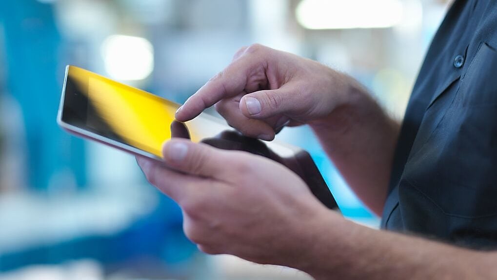 Person operating a touchscreen smartphone in an industrial setting.