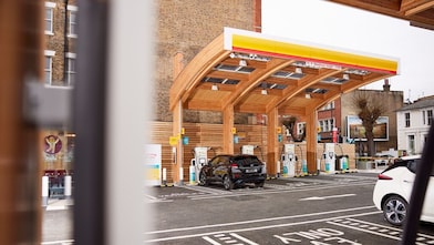 Modern electric vehicle charging station with wooden architecture and multiple charging units, with a car parked for charging.