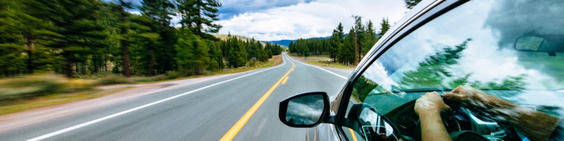 a wide expanse of empty road with a glimpse of a person driving in a car on the right