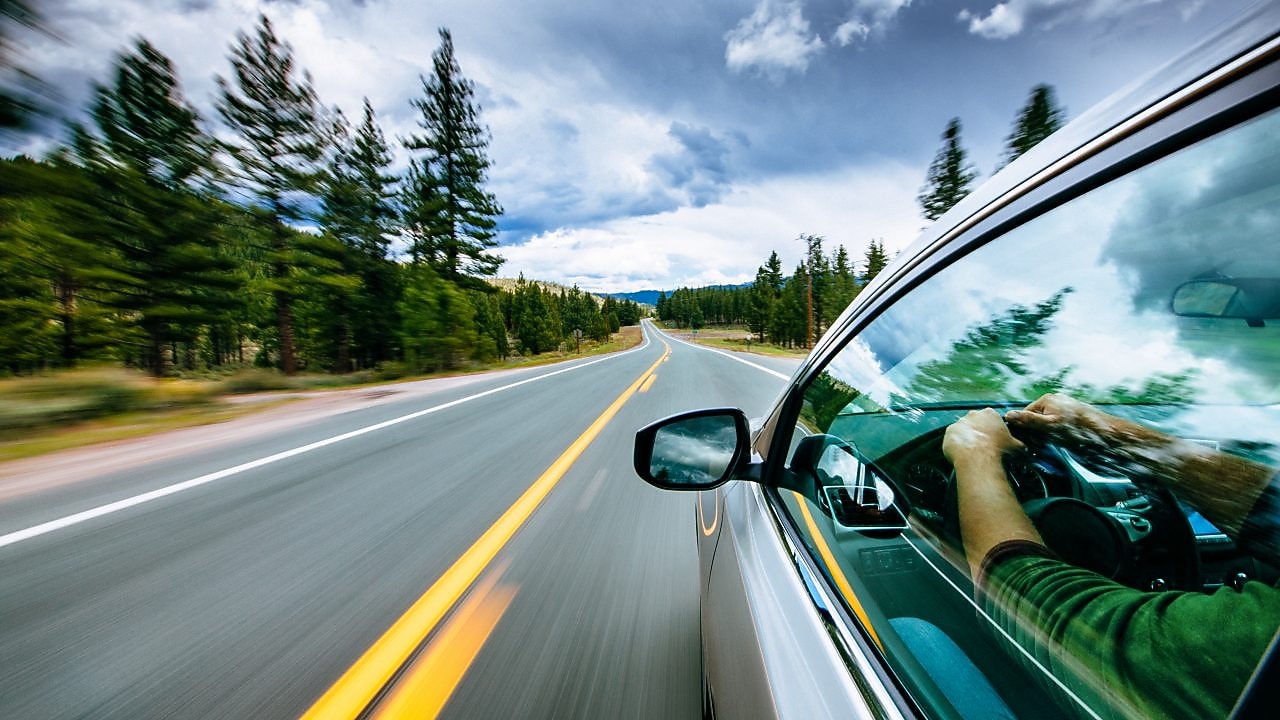 a wide expanse of empty road with a glimpse of a person driving in a car on the right