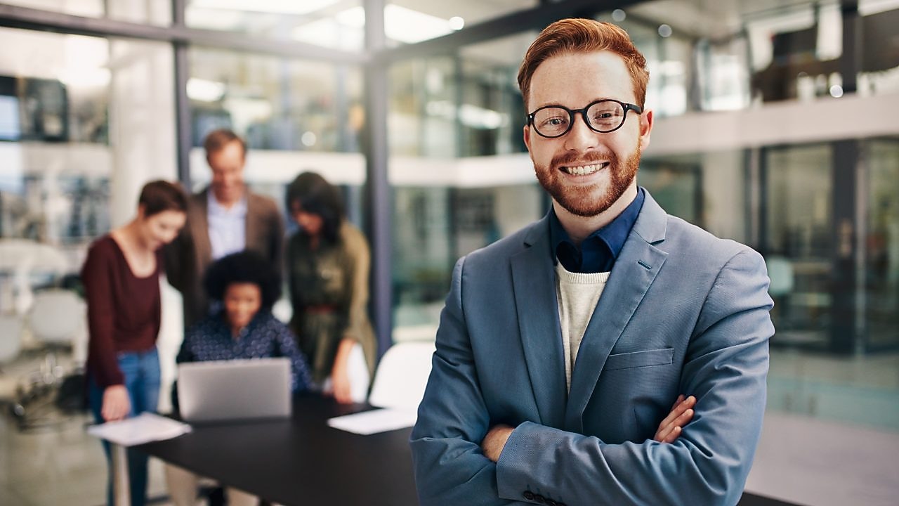 Man smiling and people watching laptop in background