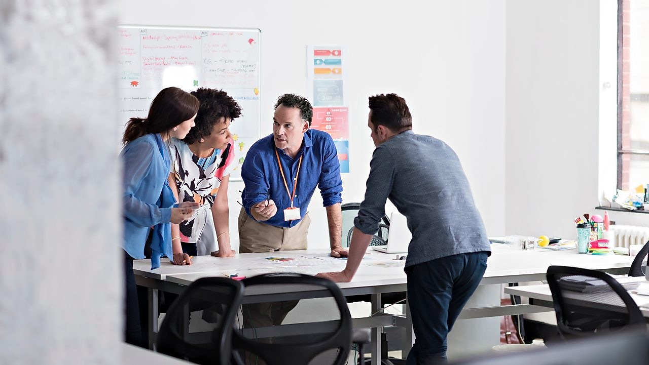 4 employees standing around a table in an office room discussing a project
