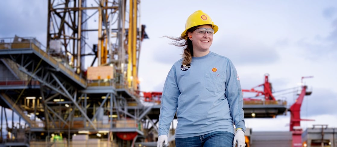 image showing a female in the foreground of an offshore platform. The female is wearing Shell branded workwear including protective headwear.