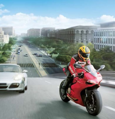 Red motorcycle and rider on a road with cars and buildings in the background