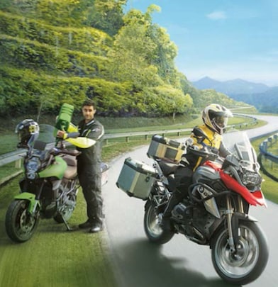 two riders, one driving on the road, one filling up motorcycle with fuel