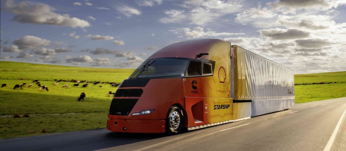side view of the Starship 3.0 truck driving by a field of cows.
