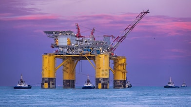 Offshore oil platform illuminated at sunset over the ocean.