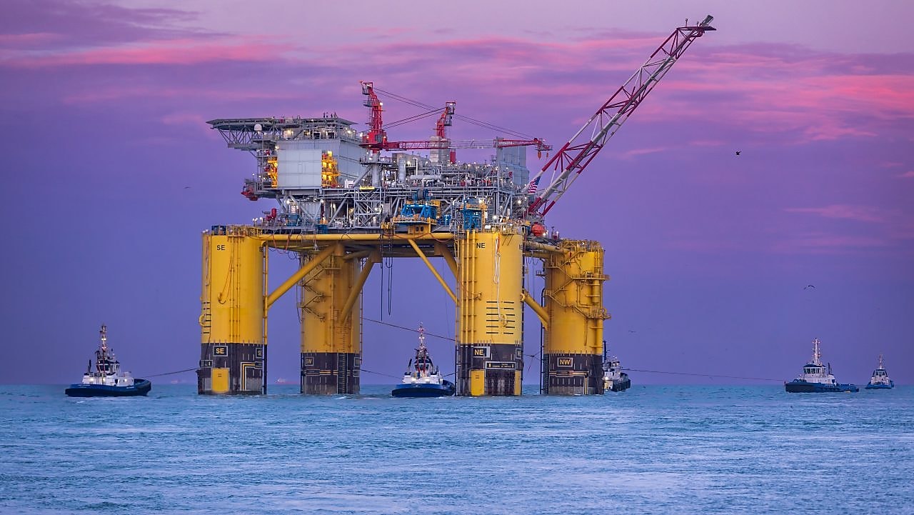 Offshore oil platform illuminated at sunset over the ocean.
