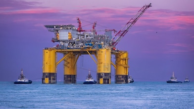 Offshore oil platform illuminated at sunset over the ocean.