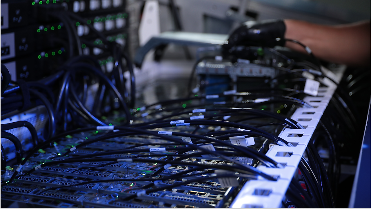 A gloved hand next to an assortment of wires connecting to a computer system.