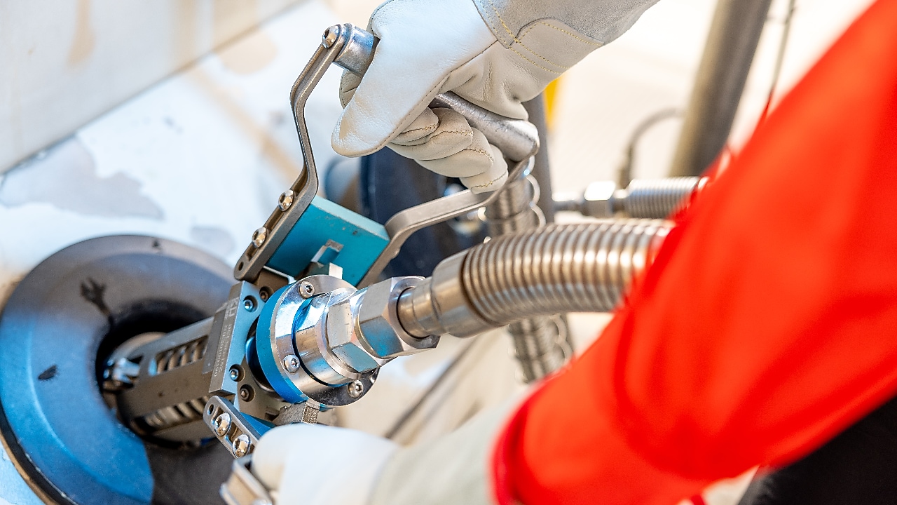 Close-up of a Shell station worker wearing gloves and a red uniform, removing an LNG fuelling nozzle from a dispenser.