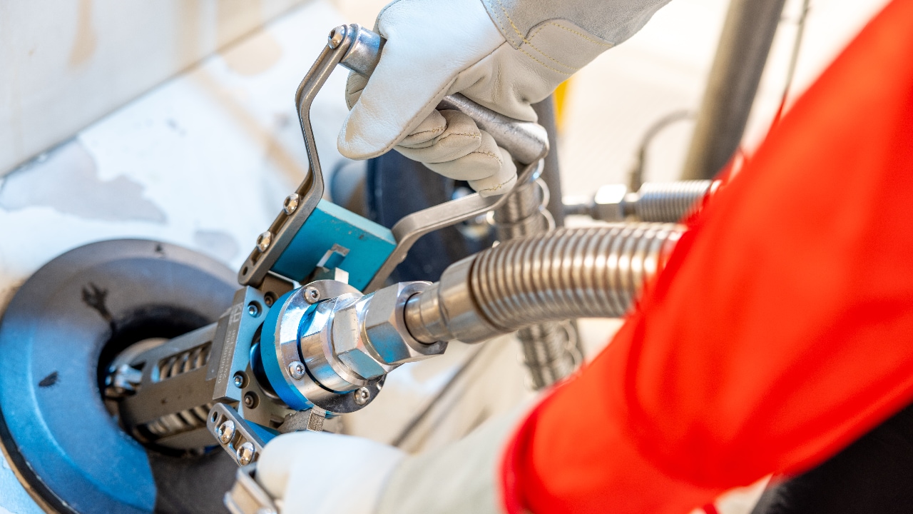 Close-up of a Shell station worker wearing gloves and a red uniform, removing an LNG fuelling nozzle from a dispenser.