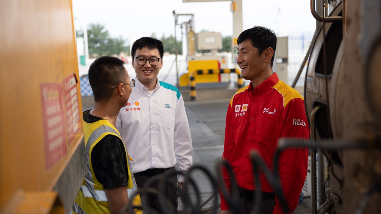 A truck driver and two Shell station workers standing near a truck at an LNG fuelling station, engaged in conversation.