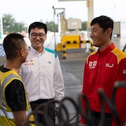 A truck driver and two Shell station workers standing near a truck at an LNG fuelling station, engaged in conversation.