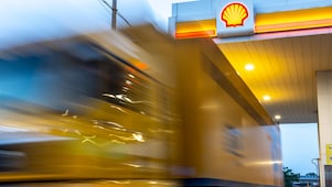A yellow express delivery truck in motion at a Shell fuelling station, with the Shell logo visible on the canopy.