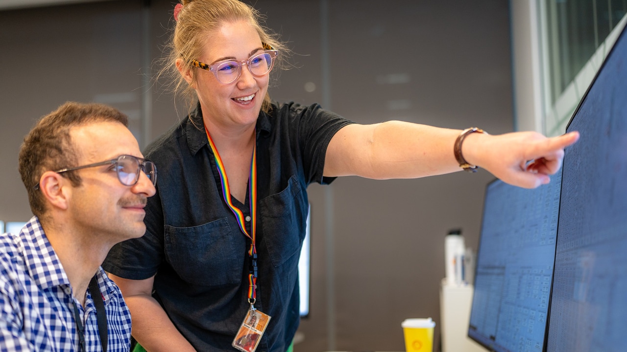 Emma Purton points towards a computer screen displaying project data in Shell's Perth office.​