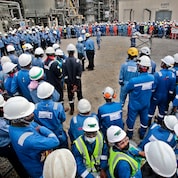 Dozens of workers wearing hard hats and blue coveralls gather at the Nigeria LNG site.