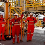 Emma stands with members of the offshore team on the Crux facility, wearing safety coveralls and hard hats among industrial equipment and walkways.