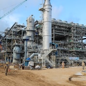 Industrial structures, cranes and scaffolding stand at the Nigeria LNG Train 7 construction site, with workers moving around the facility.