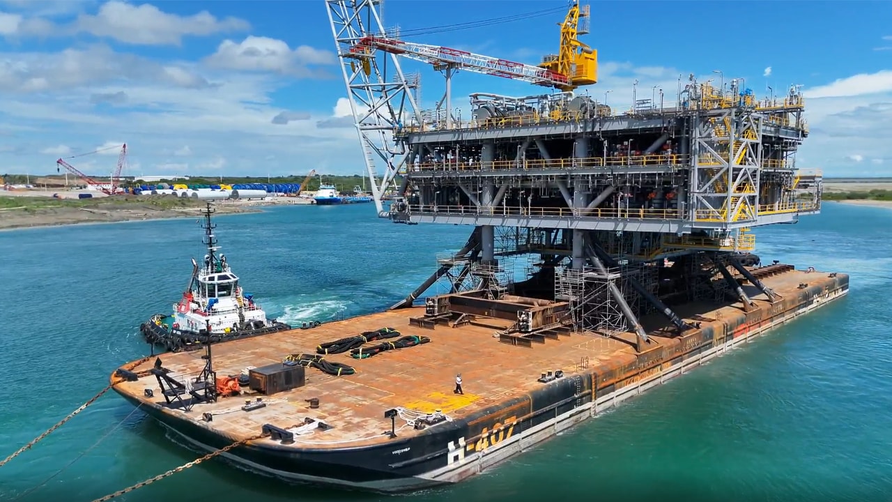Manatee platform topsides secured on a large transport barge in turquoise water off Altamira, Mexico, with a tugboat alongside.