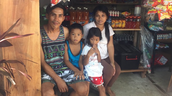 Marionito Bayonon sits with his family in the shop he’s opened which has a freezer