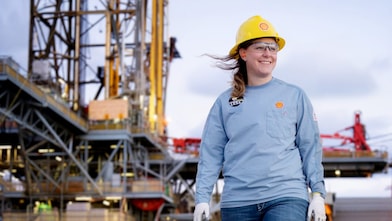 image showing a female in the foreground of an offshore platform. The female is wearing Shell branded workwear including protective headwear.