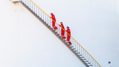 Photo of three workers wearing protective workwear holding the handrail and walking up a staircase at an oil refinery.