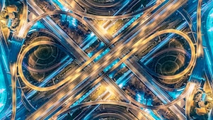 An aerial view of a network of intersecting roads at night with striking blue and yellow colours added to light up parts of the roads.