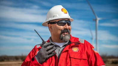 A Shell employee wearing Shell branded protective workwear uses his radio during maintenance work on a wind turbine.