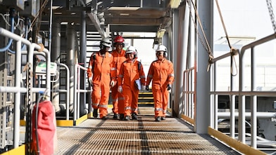 Four people wearing protective workwear walking together in conversation at a production facility.