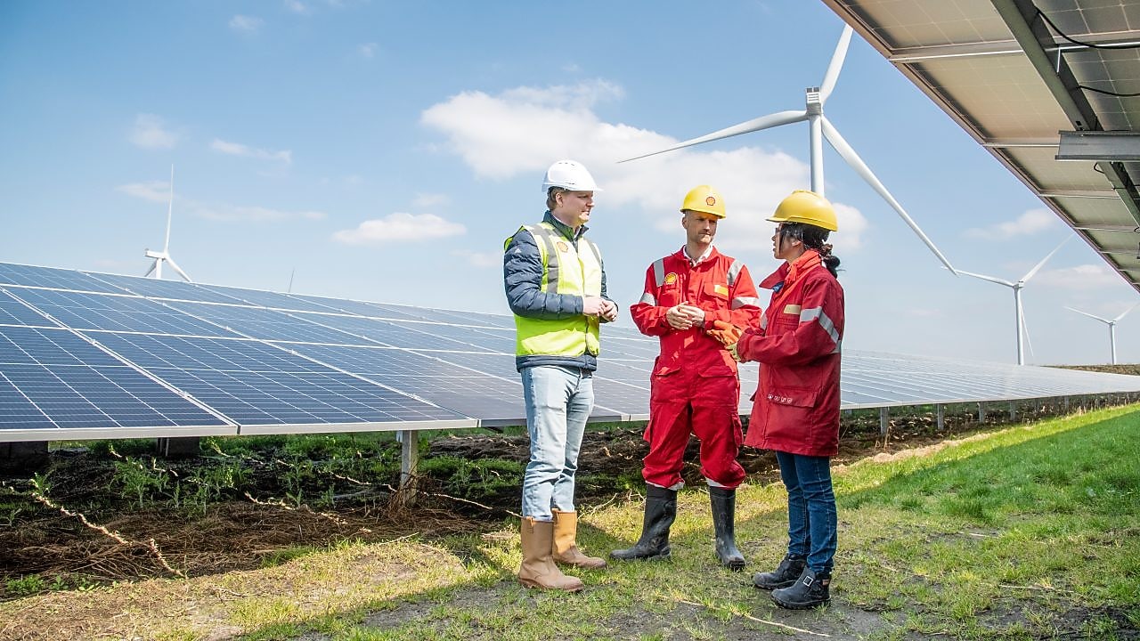 three people in hard hats speaking amidst a field of solar panels