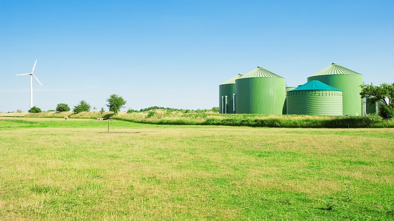 biogas and wind turbine seen against a blue sky and green agricultural field