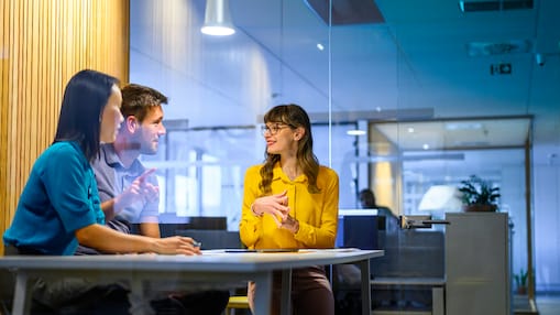 3 people talking at a table in a glass meeting room