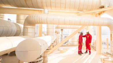 Two men in red suits under pipelines