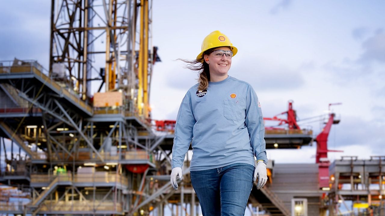 image showing a female in the foreground of an offshore platform. The female is wearing Shell branded workwear including protective headwear.