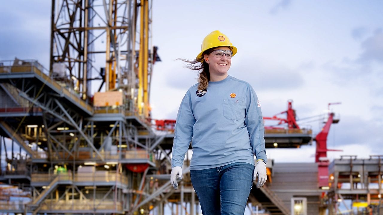 image showing a female in the foreground of an offshore platform. The female is wearing Shell branded workwear including protective headwear.