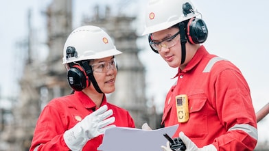 Two workers in protective gear reviewing plans at an industrial site.