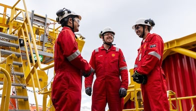 Three Shell employees stand onboard a processing vessel. All are wearing Shell branded protective workwear.