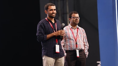 two men at a stage, speaking to a microphone