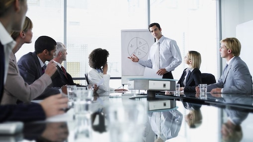 A gentelman presenting in a meeting room to a group of people.
