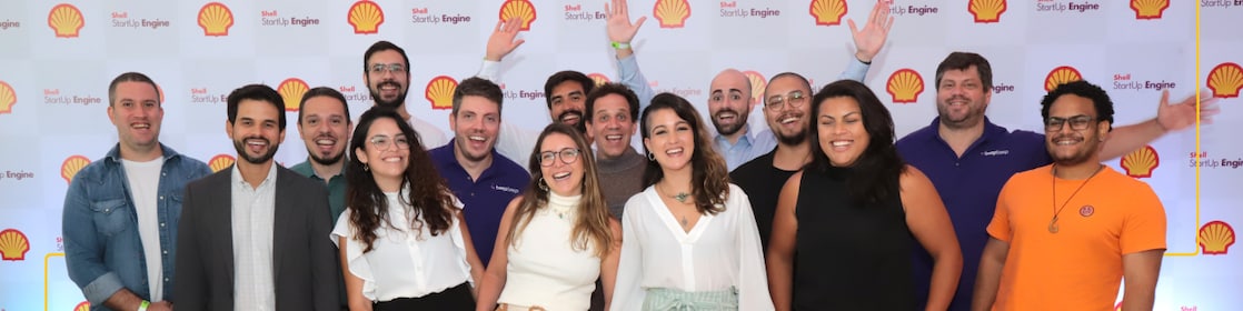 Thirteen people are posing for a group photo in front of a backdrop featuring the Shell logo and "Shell StartUp Engine" text. 