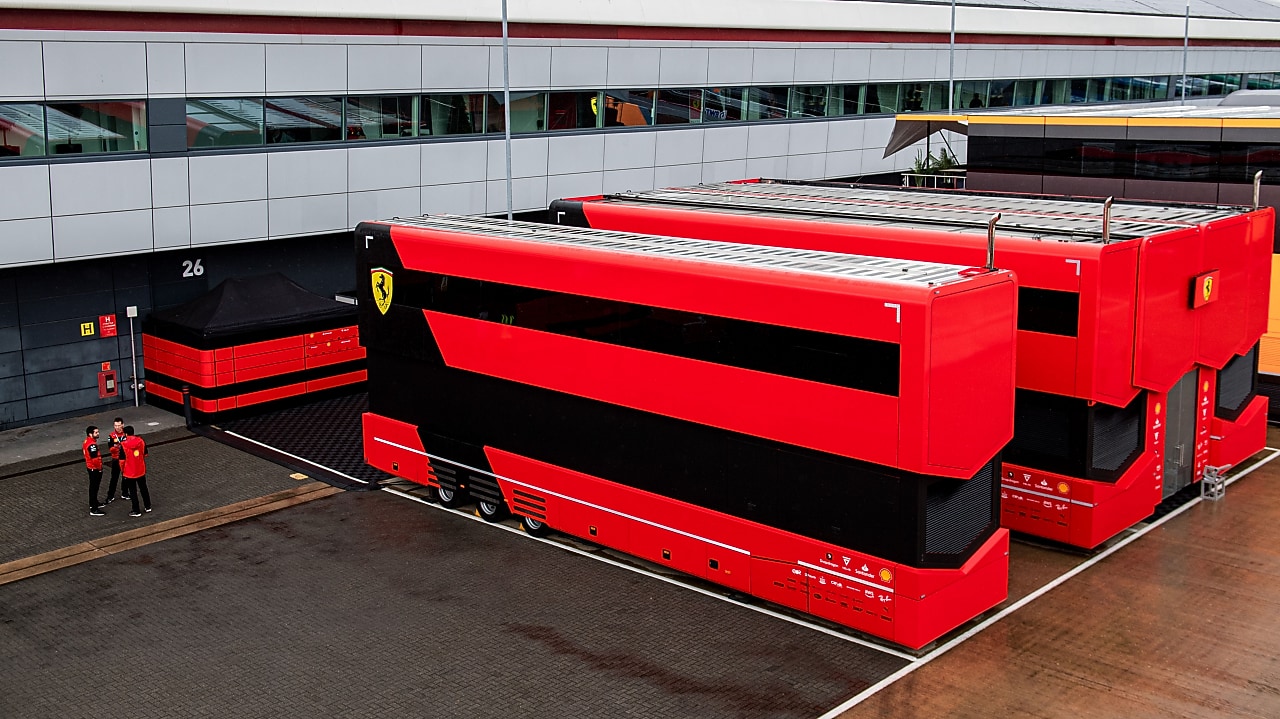 An elevated view of the Ferrari motorhomes seen at F1 circuits. On the left hand side are 3 Ferrari employees talking to each other in a circle.