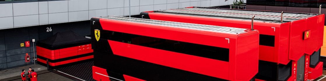 An elevated view of the Ferrari motorhomes seen at F1 circuits. On the left hand side are 3 Ferrari employees talking to each other in a circle.