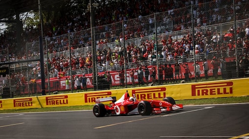Ferrari F2002 car driving around the Monza circuit, photographed from a distance with trackside barriers in the background.