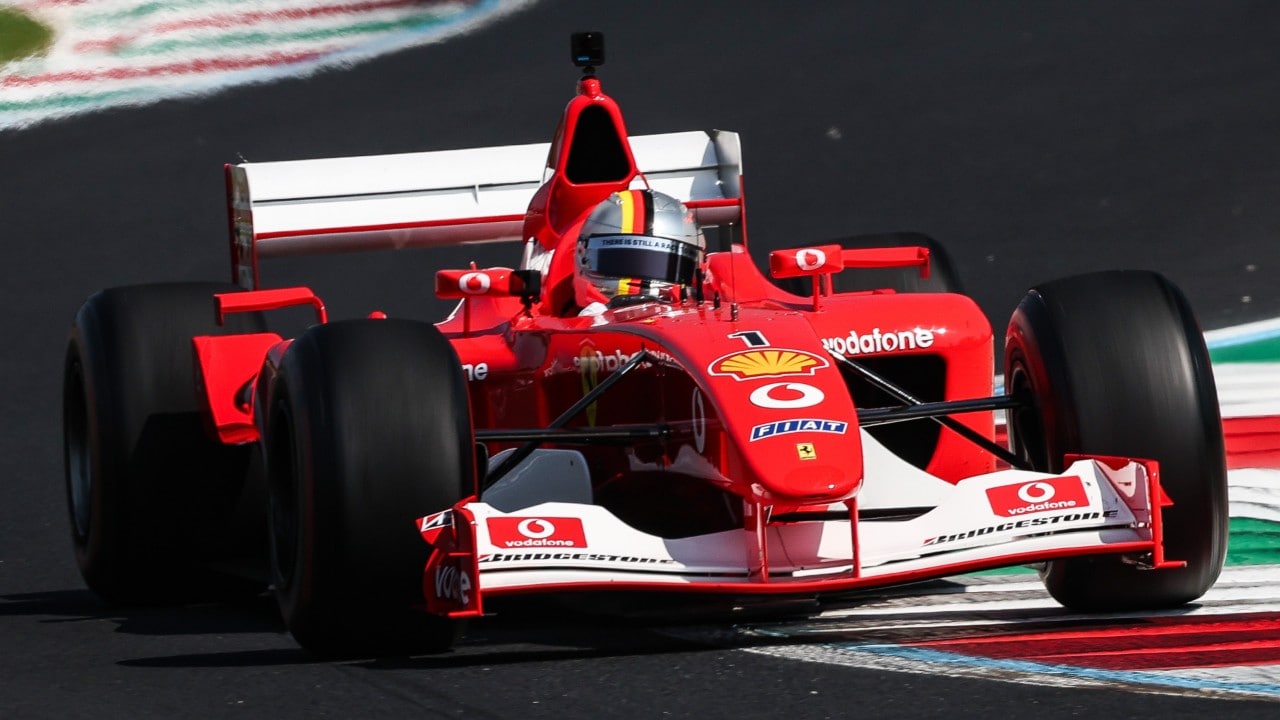 Front view of the Ferrari F2002 car navigating the Monza circuit, with red, white and green kerbing alongside the track.