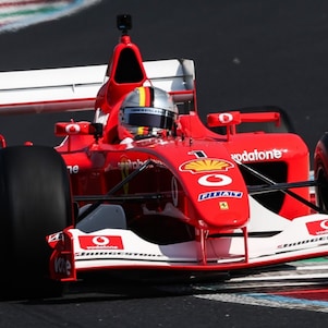 Front view of the Ferrari F2002 car navigating the Monza circuit, with red, white and green kerbing alongside the track.