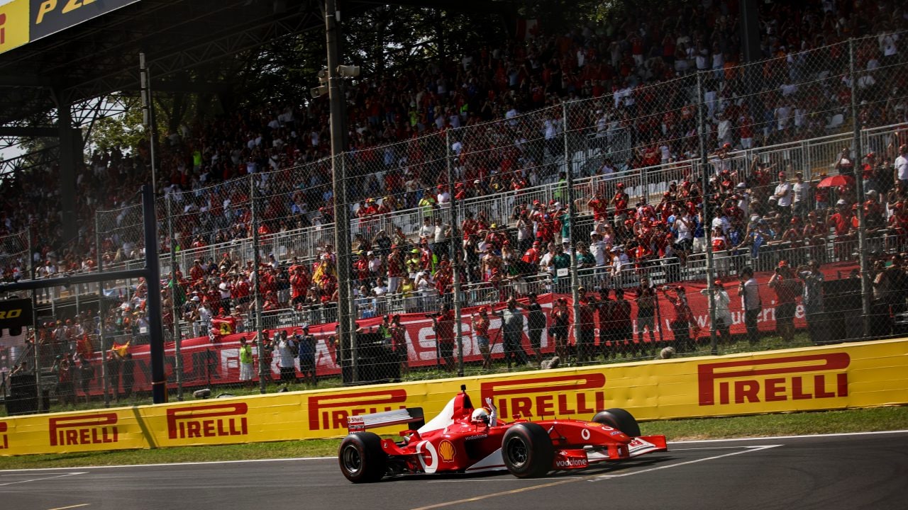 Ferrari F2002 car driving around the Monza circuit, photographed from a distance with trackside barriers in the background.