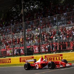Ferrari F2002 car driving around the Monza circuit, photographed from a distance with trackside barriers in the background.