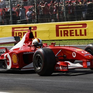 Ferrari F2002 car driving on the Monza circuit in front of trackside barriers and spectators.